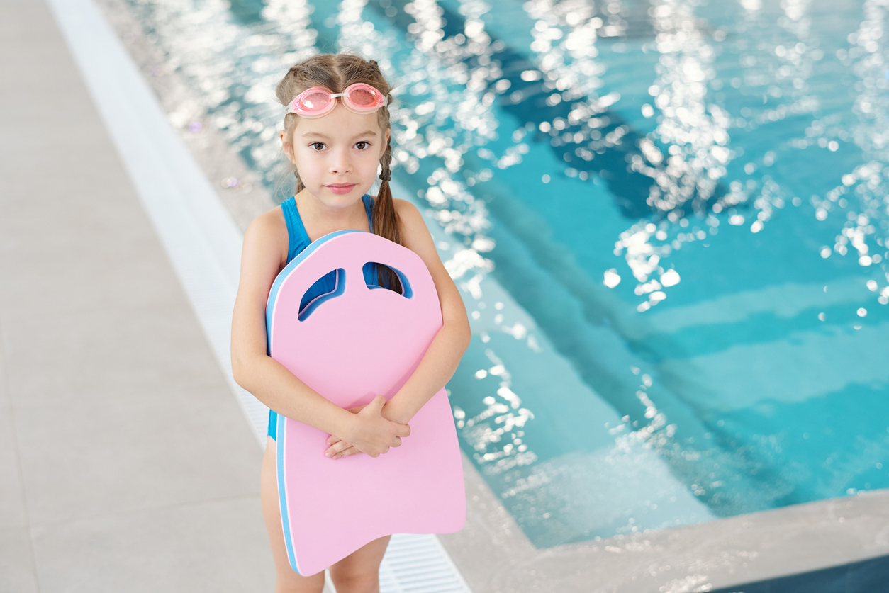 Adorable Little Girl In Swimwear And Goggles Standing Against Swimming Pool